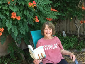 Minrose Gwin sitting in a chair holding a book with a trumpet creeper vine flowering behind her